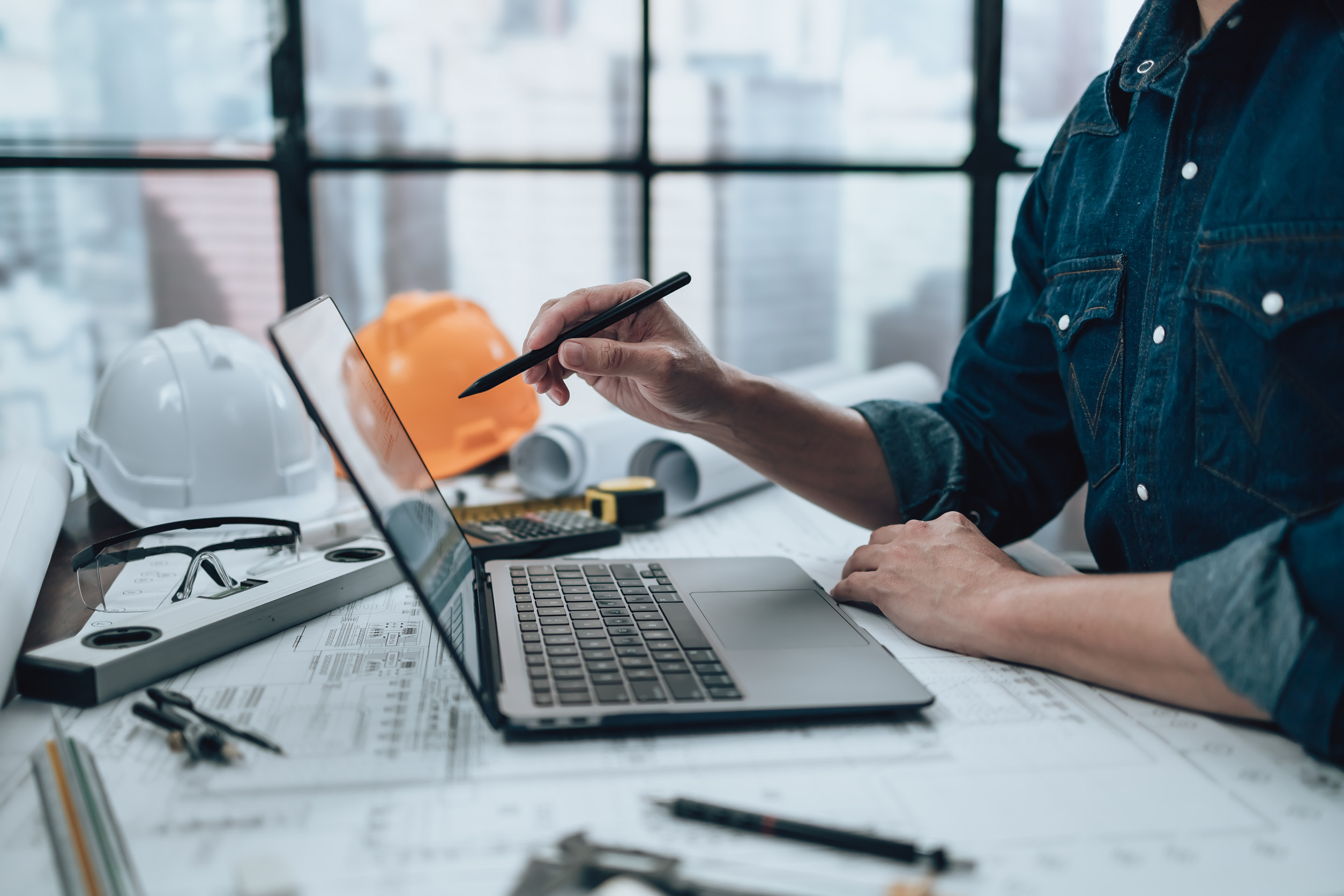 Ingénieur travaillant sur ordinateur avec plans architecturaux.